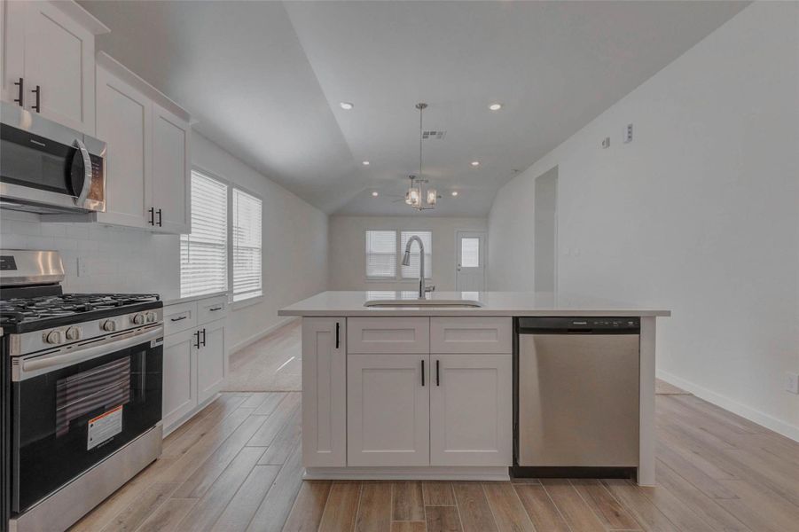 This angle showcases the expansive quartz island as the heart of the home linking the gourmet kitchen to the open living and dining areas. From every vantage point, this space feels connected and bright, offering clean lines, soft tones, and stylish lighting that make it move-in ready and design-forward.