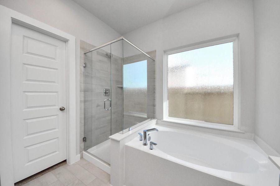 Indulge in a spa-like retreat within the confines of this primary bathroom. Delight in a spacious walk-in shower enveloped in stylish tile surround, unwind in a separate garden tub adorned with custom detailing. Sample photo of completed home with similar floor plan. Actual colors and selections may vary.