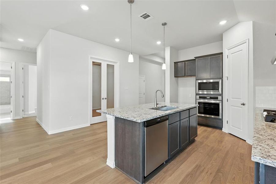 Kitchen featuring stainless steel appliances, light stone countertops, light wood-style floors, and a center island with sink