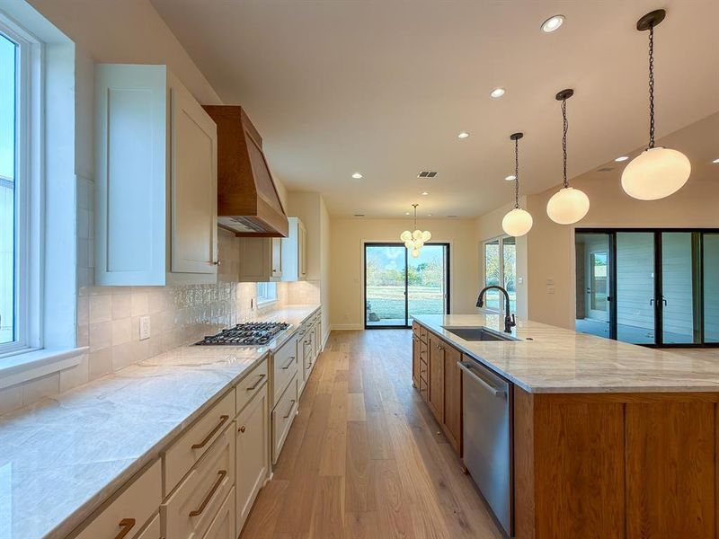 Spacious kitchen featuring an extended island, light wood-finish flooring, white cabinetry, a wood range hood, and a gas cooktop