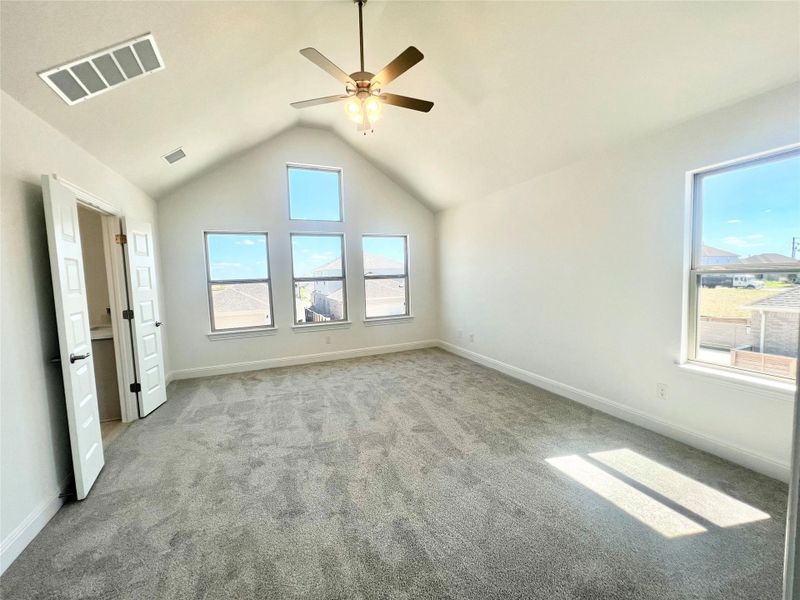 Unfurnished bedroom featuring carpet floors, multiple windows, vaulted ceiling, and a ceiling fan
