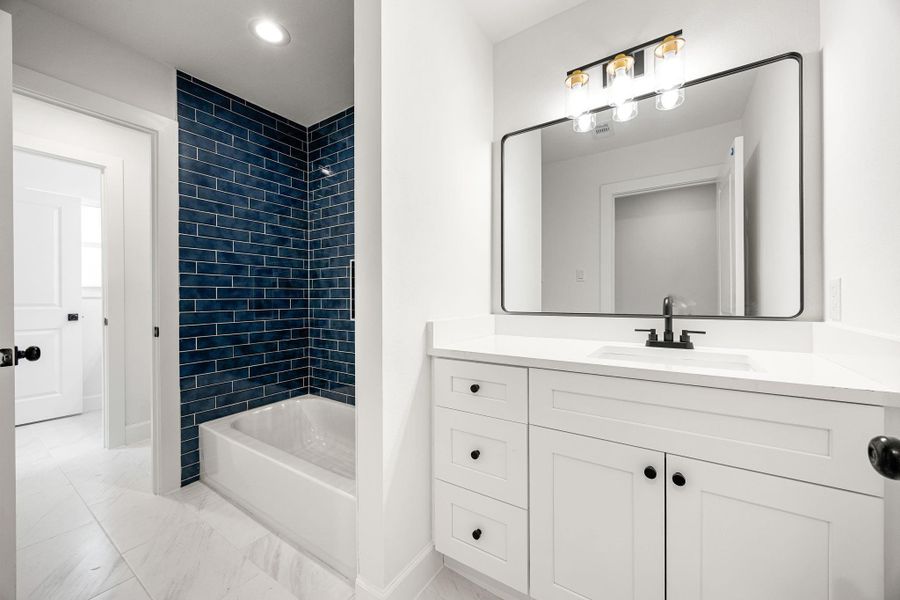 Modern bathroom featuring a sleek white vanity with quartz countertop, black hardware, and a large framed mirror with contemporary lighting. The space is complemented by stylish tile flooring and a tub/shower combo with striking dark tile accent for a bold, modern touch.
