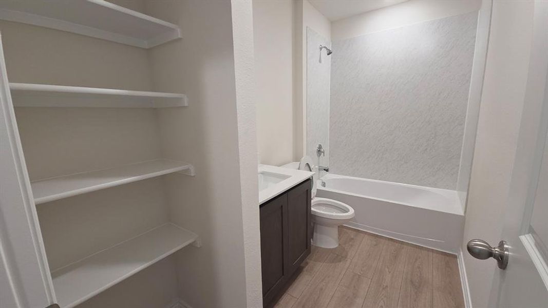 Bathroom featuring a dark wood-finish vanity with an integrated sink, a white toilet, and a white bathtub with a textured shower surround Bathroom featuring a dark wood-finish vanity with an integrated sink, a white toilet, and a white bathtub with a textured shower surround