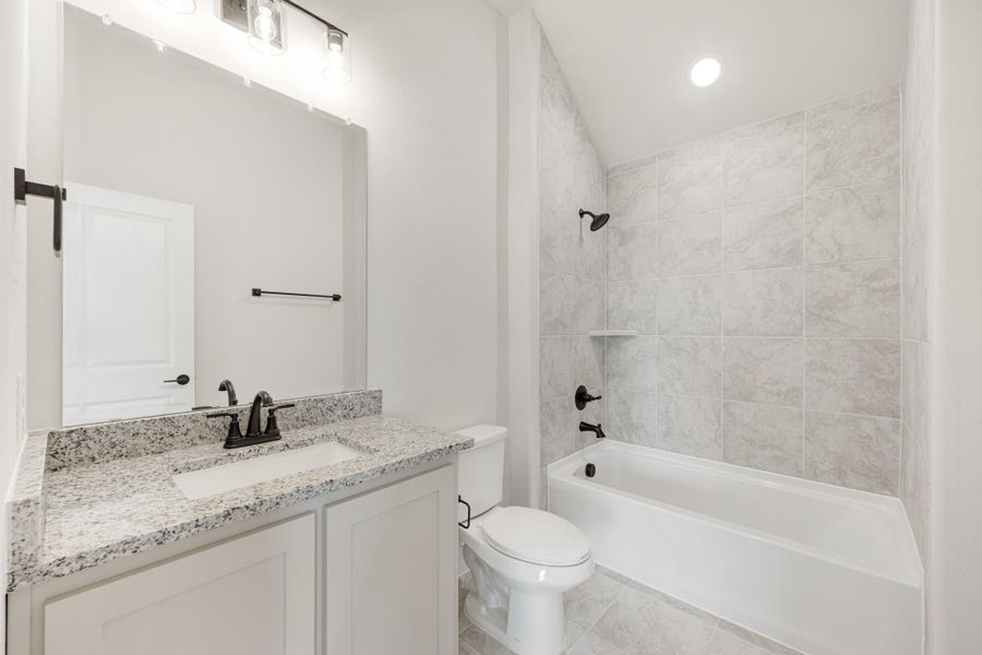 Bathroom with granite countertop vanity, white tub, and tiled shower surround with dark fixtures
