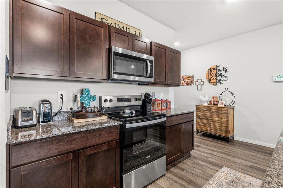 Kitchen featuring stainless steel appliances, dark stone counters, dark wood finish cabinetry, and dark wood-style flooring