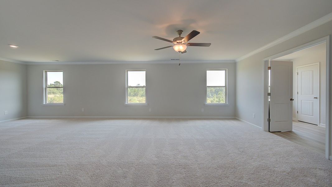 Expansive primary suite with carpet flooring, overhead fan light, and connecting bath in the Clarity at Brighton.
