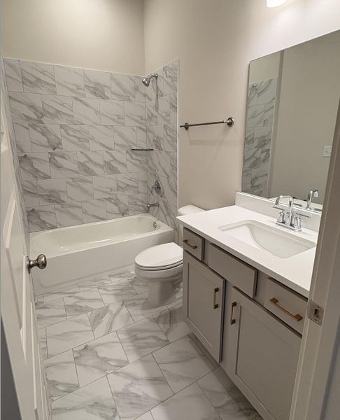 Full bath with light marble finish floors, vanity, and shower / bath combination