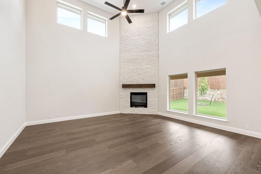 Open living room with floor-to-ceiling stone fireplace, dark hardwood floors, and high ceilings with ceiling fan Open living room with floor-to-ceiling stone fireplace, dark hardwood floors, and high ceilings with ceiling fan