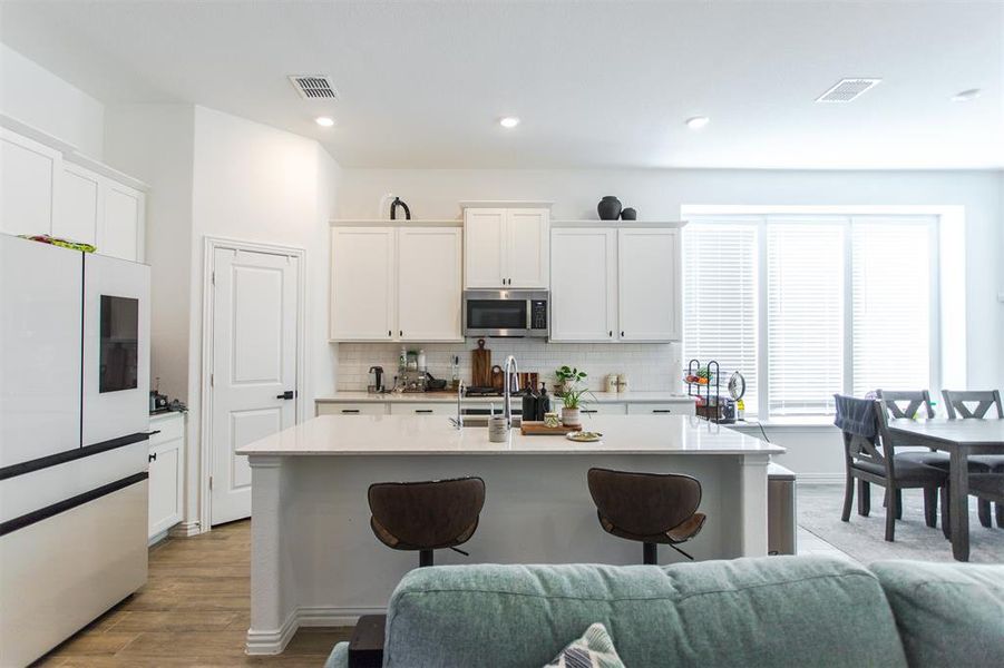 Kitchen with tasteful backsplash, a kitchen island with sink, white cabinets, and light wood-type flooring