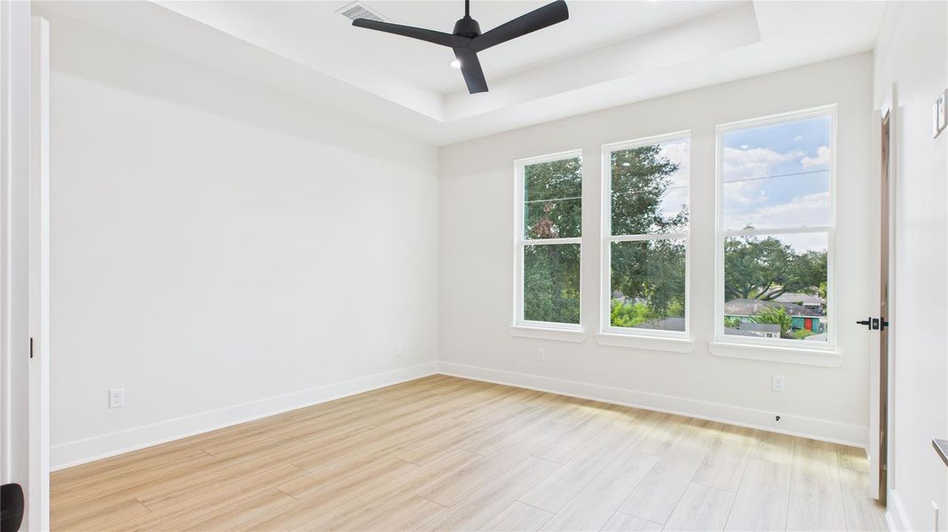 Bright and spacious primary bedroom with large windows, light wood flooring, and a modern ceiling fan.