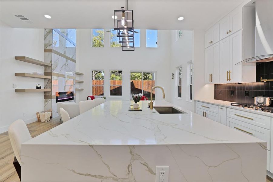 Kitchen featuring a sink, wall chimney exhaust hood, stainless steel gas stovetop, a chandelier, and a center island with sink