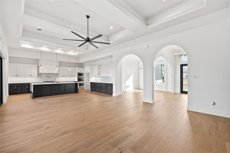 Unfurnished living room with a raised ceiling, light wood-style floors, a chandelier, a ceiling fan, and arched walkways Unfurnished living room with a raised ceiling, light wood-style floors, a chandelier, a ceiling fan, and arched walkways
