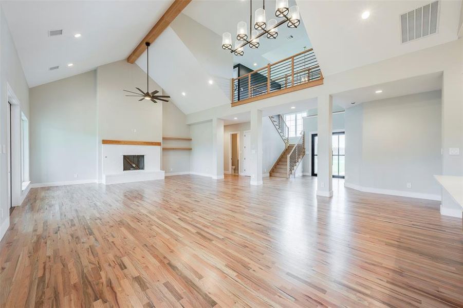 Unfurnished living room with beam ceiling, a fireplace with raised hearth, light wood-type flooring, high vaulted ceiling, and stairway
