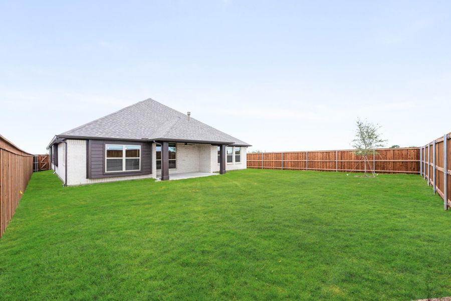 Backyard with large green lawn, covered patio, and wood privacy fence surrounding single-story home Backyard with large green lawn, covered patio, and wood privacy fence surrounding single-story home
