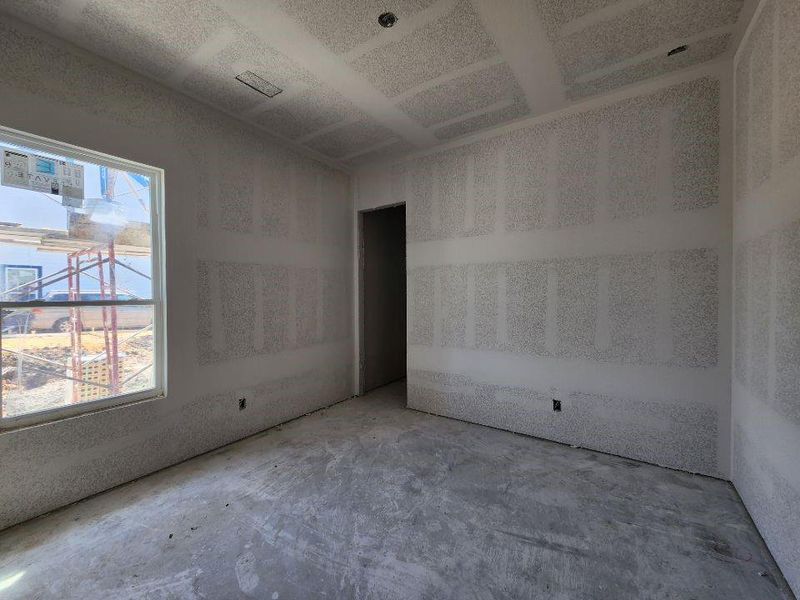 Unfinished interior room featuring a large window, a framed doorway, exposed drywall, and a concrete subfloor