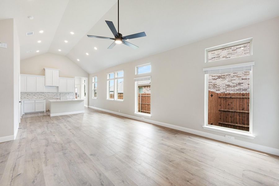 Open living area with vaulted ceiling, ceiling fan, hardwood floors, and open kitchen with white cabinets in background