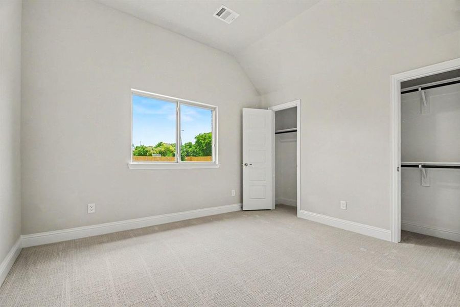 Spacious room featuring vaulted ceilings, light-colored carpeting, a large window, and two separate closets with built-in shelving and hanging rods Spacious room featuring vaulted ceilings, light-colored carpeting, a large window, and two separate closets with built-in shelving and hanging rods