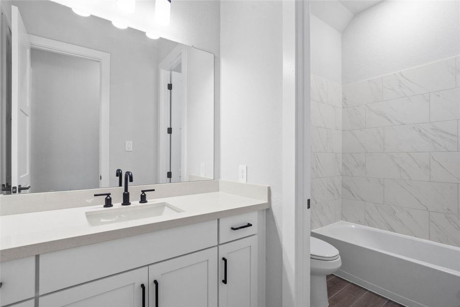 Secondary bathroom features a vanity with quartz countertops and sleek finishes. The tub/shower combination with tile surround and toilet can be closed off with the convenient pocket door for added privacy!