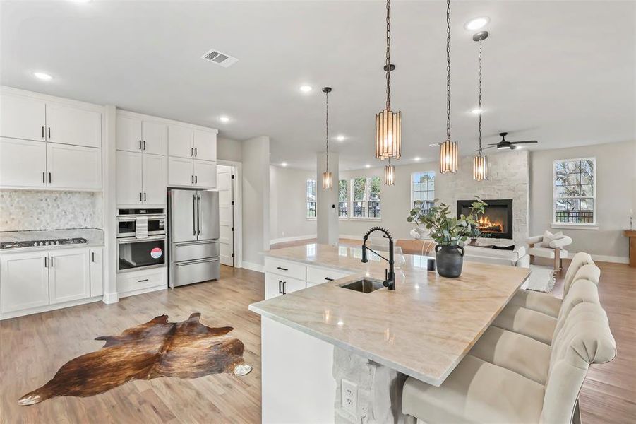 Kitchen featuring white cabinetry, light wood-type flooring, hanging light fixtures, light stone counters, and recessed lighting Kitchen featuring white cabinetry, light wood-type flooring, hanging light fixtures, light stone counters, and recessed lighting