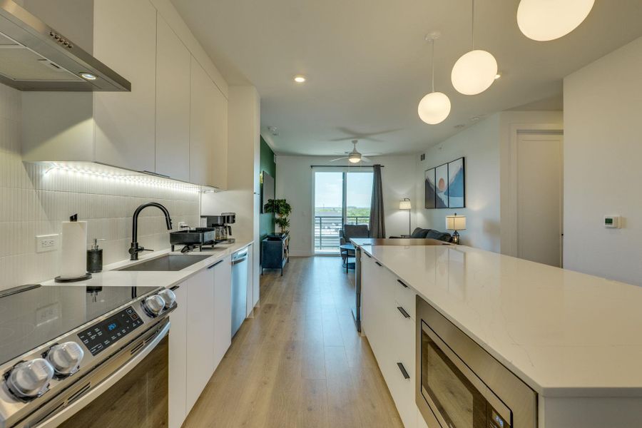 The kitchen features white cabinetry, a stainless steel range with a ventilation hood, a black sink faucet, and under-cabinet lighting