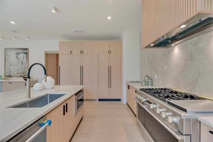 Kitchen featuring stainless steel appliances, ventilation hood, sink, light hardwood / wood-style flooring, and light brown cabinets