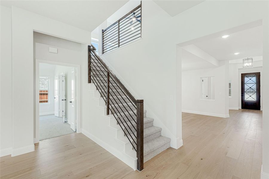 Open foyer with staircase featuring dark wood and metal railing, light hardwood floors, and front entry door with glass panels