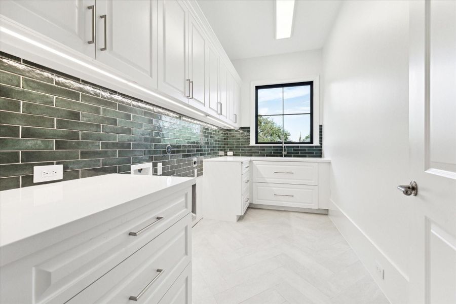 [Laundry / Utility Room]Located on the second floor; note subway tile backsplash, abundant counter, cabinet, and drawer storage, and sink.