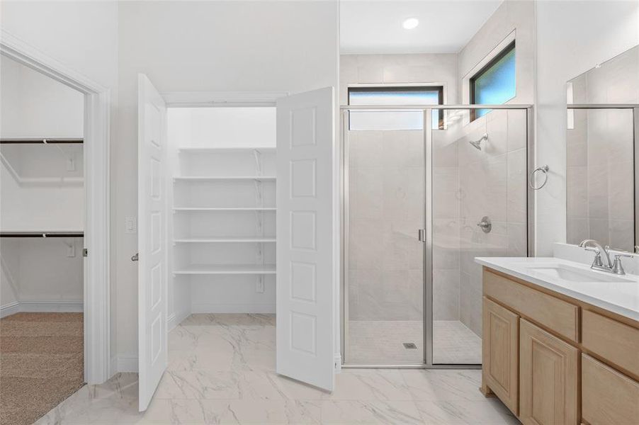 Full bathroom featuring a spacious closet, vanity, a shower stall, and light marble finish flooring Full bathroom featuring a spacious closet, vanity, a shower stall, and light marble finish flooring