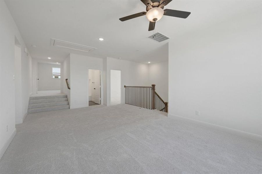 Carpeted open area with a ceiling fan, recessed lighting, white walls, and a wooden staircase