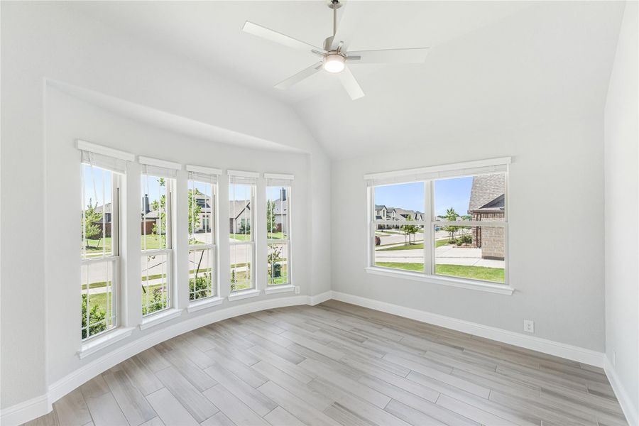 Bright empty room with vaulted ceiling, ceiling fan, large windows, and light wood-look floors