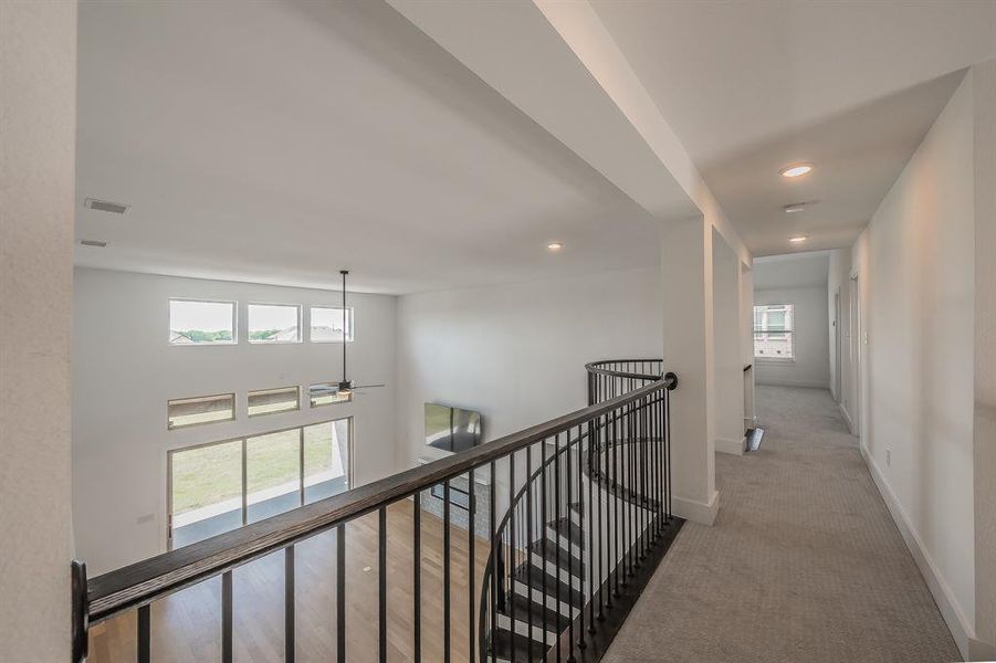 Upper level featuring a carpeted hallway with recessed lighting and a view overlooking the lower level with hardwood floors, a ceiling fan, and large windows