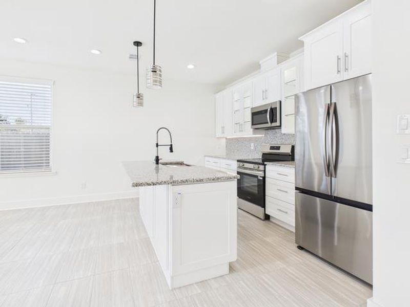 Kitchen with appliances with stainless steel finishes, hanging light fixtures, an island with sink, light stone counters, and white cabinets Kitchen with appliances with stainless steel finishes, hanging light fixtures, an island with sink, light stone counters, and white cabinets