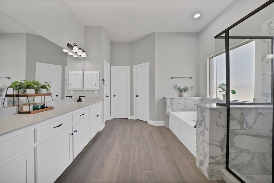 Bathroom featuring a garden tub, vanity, a marble finish shower, wood finished floors, and baseboards Bathroom featuring a garden tub, vanity, a marble finish shower, wood finished floors, and baseboards