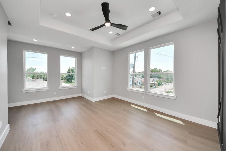 Spacious primary bedroom featuring tray ceilings, oversized windows, abundant natural light, & modern finishes throughout.