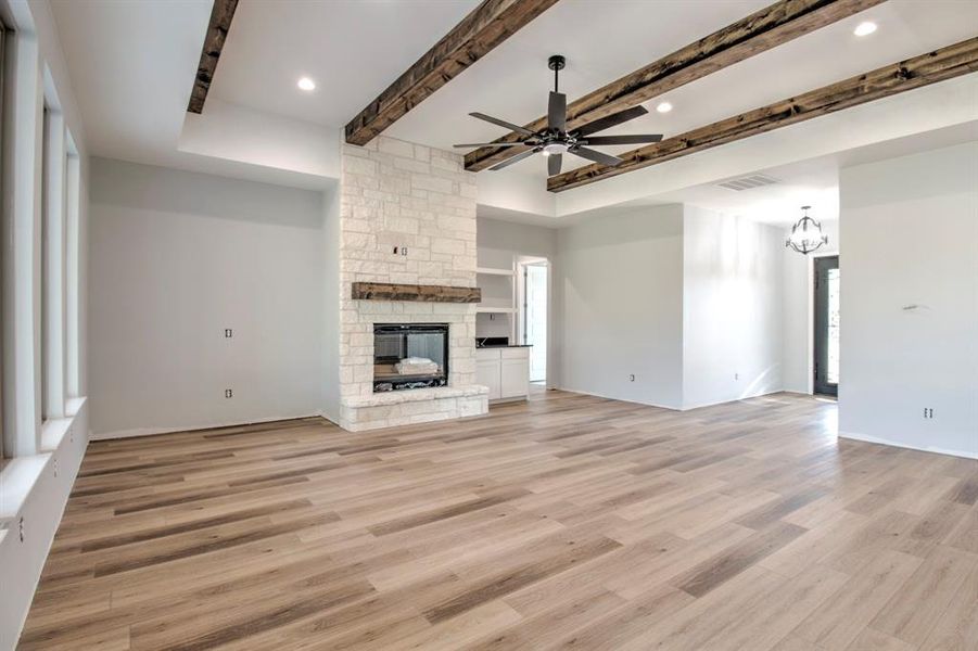 Unfurnished living room with ceiling fan with notable chandelier, beamed ceiling, light hardwood / wood-style flooring, and a fireplace