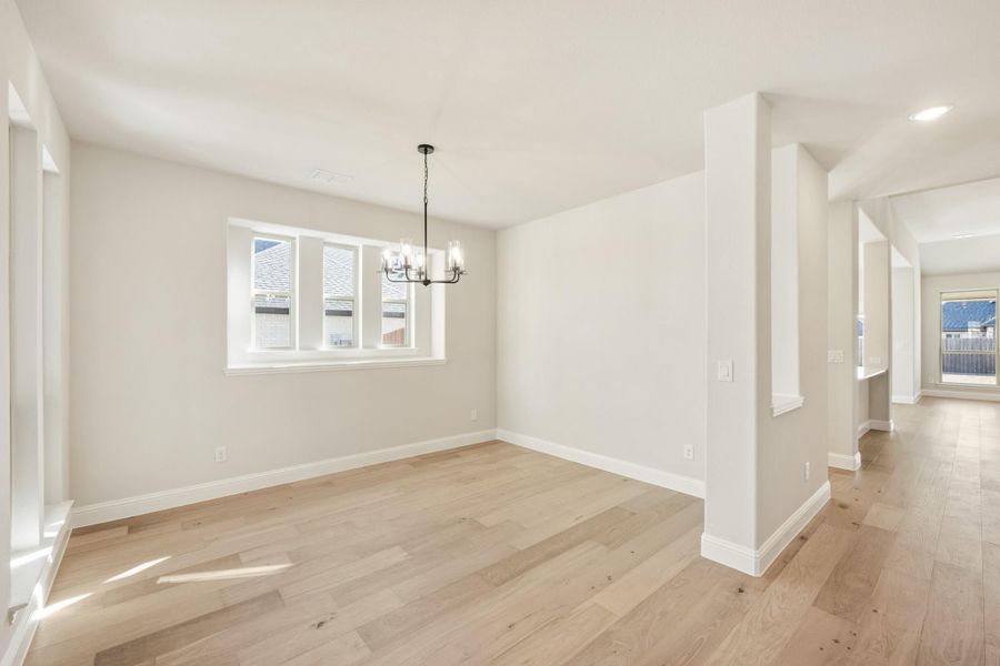 Empty dining room with light hardwood floors, chandelier, and large window overlooking neighborhood