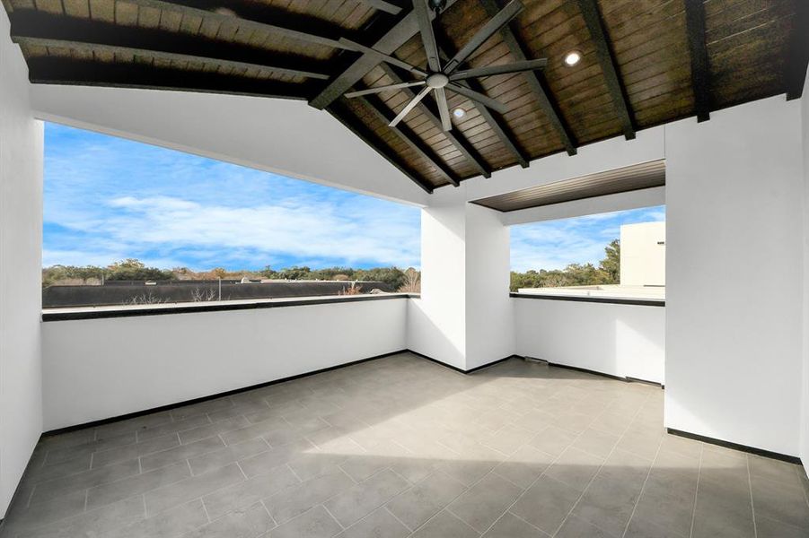 Expansive 3rd-floor rooftop terrace with a vaulted wood ceiling, modern fan, covered design, and sleek tile flooring. Enjoy panoramic views in a space perfect for outdoor living and entertaining