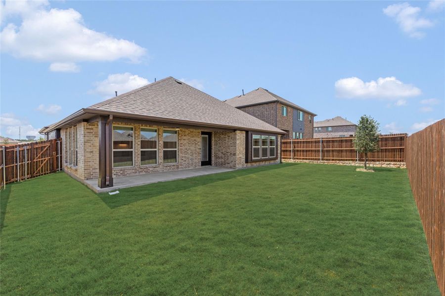 Brick home rear exterior with covered patio, large fenced backyard, and green lawn Brick home rear exterior with covered patio, large fenced backyard, and green lawn