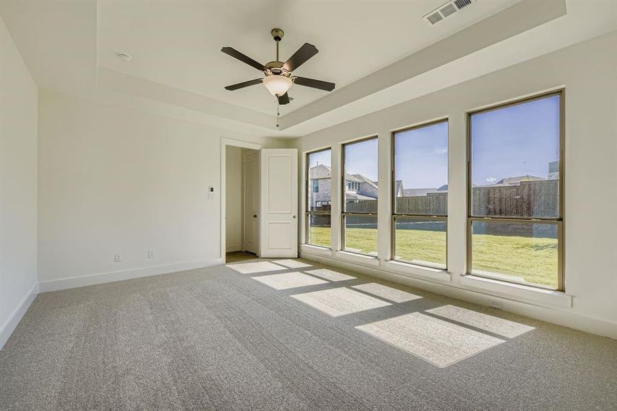 Spare room with a raised ceiling, light colored carpet, and a ceiling fan Spare room with a raised ceiling, light colored carpet, and a ceiling fan