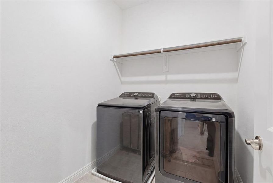 Dedicated laundry area featuring a white wall shelf, wooden hanging rod, and light-toned flooring Dedicated laundry area featuring a white wall shelf, wooden hanging rod, and light-toned flooring