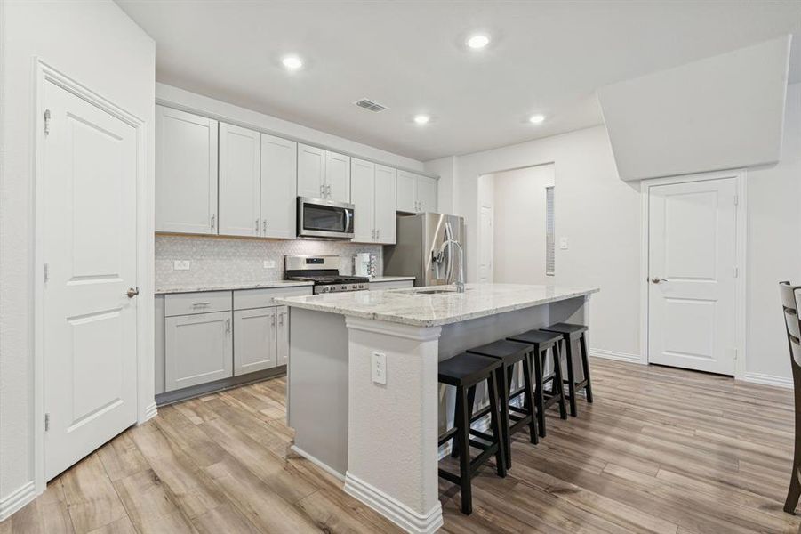 Kitchen with a breakfast bar area, appliances with stainless steel finishes, an island with sink, light stone countertops, and decorative backsplash