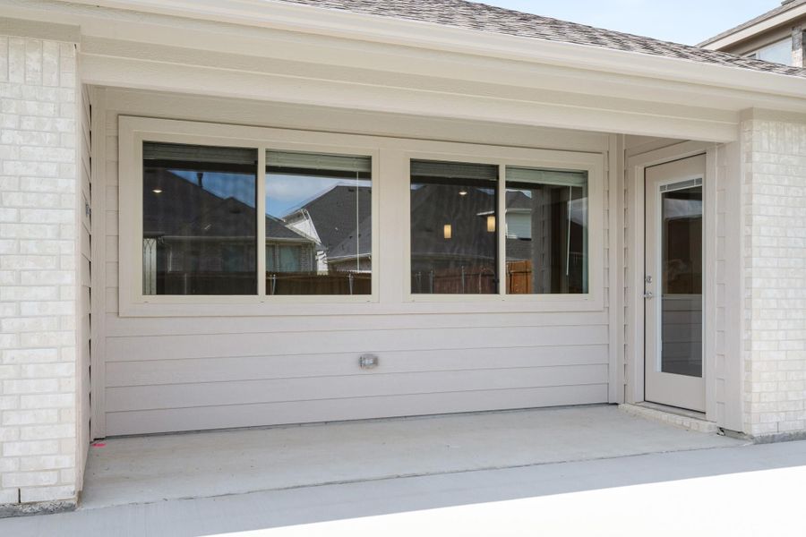 Covered patio with large windows, side entry door, and white brick exterior walls on a new home. Covered patio with large windows, side entry door, and white brick exterior walls on a new home.