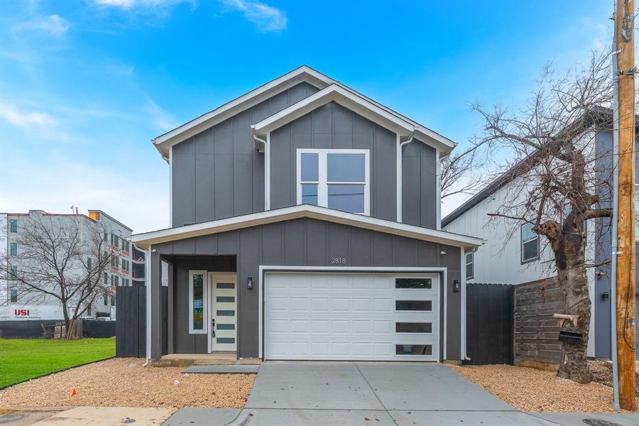 View of front of home featuring an attached garage, concrete driveway, board and batten siding, and fence