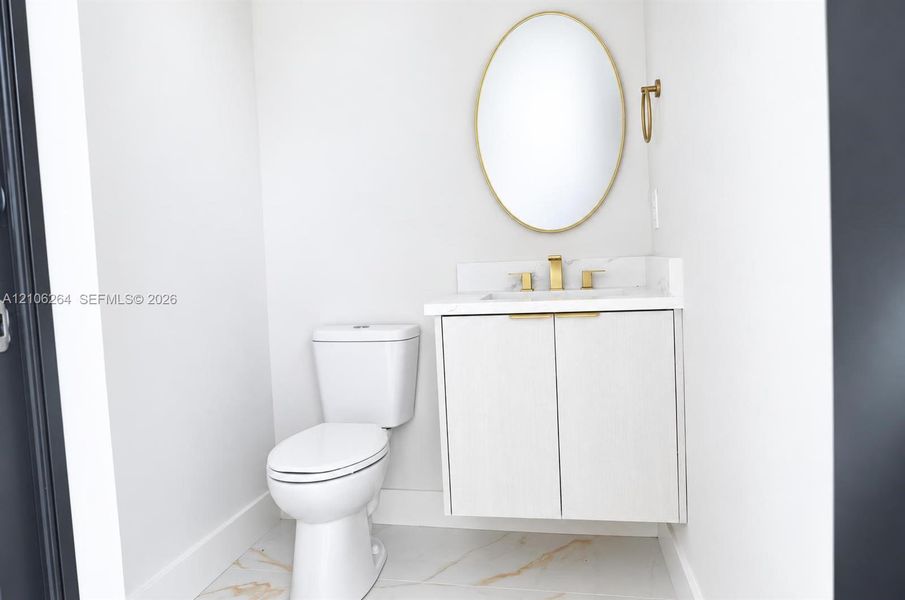 Floating vanity with integrated countertop and backsplash, brass-toned hardware, oval-framed mirror, and large-format tile flooring