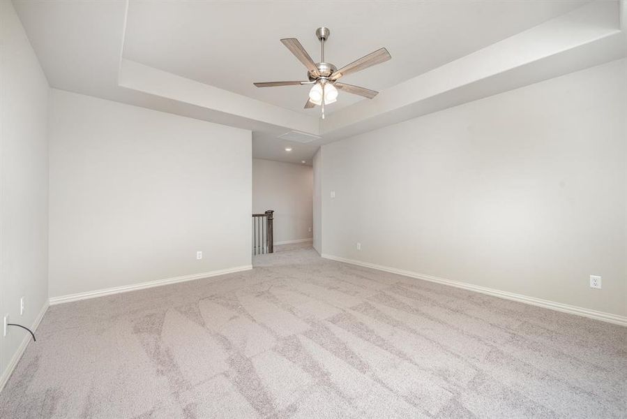 Carpeted empty room with ceiling fan and a raised ceiling