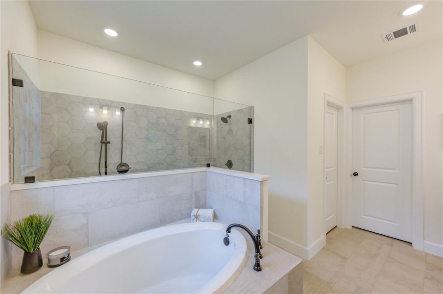 This modern bathroom features a spacious bathtub with elegant fixtures and a glass-enclosed shower. The neutral tile and hexagonal accent wall create a clean, sophisticated look, while recessed lighting adds a bright, inviting atmosphere.