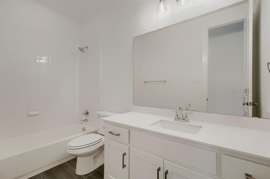 White bathroom featuring a built-in tub with a tiled surround, a white vanity with an undermount sink, a large wall-mounted mirror, and wood-finish flooring