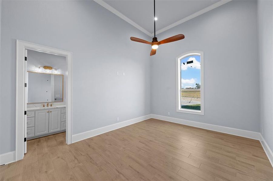 Unfurnished bedroom with light wood finished floors, crown molding, ceiling fan, a towering ceiling, and connected bathroom Unfurnished bedroom with light wood finished floors, crown molding, ceiling fan, a towering ceiling, and connected bathroom