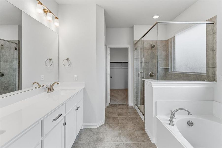 Bathroom featuring double vanity, a walk in closet, a shower stall, a bath, and light tile patterned flooring