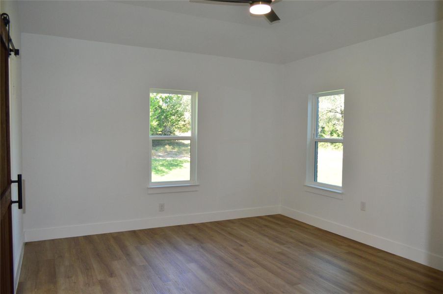 Unfurnished room with healthy amount of natural light, wood finished floors, a barn door, and ceiling fan Unfurnished room with healthy amount of natural light, wood finished floors, a barn door, and ceiling fan